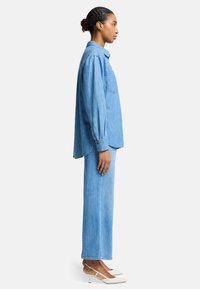 Jasnoniebieska koszula dżinsowa i dopasowane szerokie spodnie, z przednią kieszenią, luźny krój oraz spiczaste białe szpilki. Gładka textura.