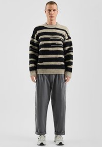 Pull en tricot rayé beige et marine avec une finition texturée, associé à un pantalon gris ample et des baskets de couleur claire.
