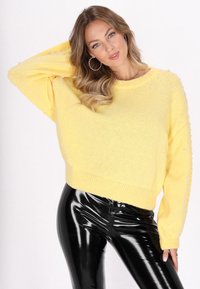 Pulover galben, supradimensionat din tricot cu embellishments de perle pe mâneci. Asortat cu leggings negri, cu finisaj lucios. Textură ușoară, croială lejeră.