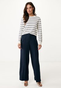 Wit gestreepte lange mouwen shirt gecombineerd met wijde marineblauwe broek. Het shirt heeft een ronde halslijn en de broek heeft een geplooide voorkant en een rechte snit.