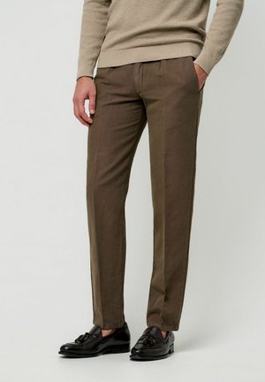 Braune Baumwollhose mit geradem Schnitt, zwei Seitentaschen und glatter Textur, kombiniert mit schwarzen Loafers.