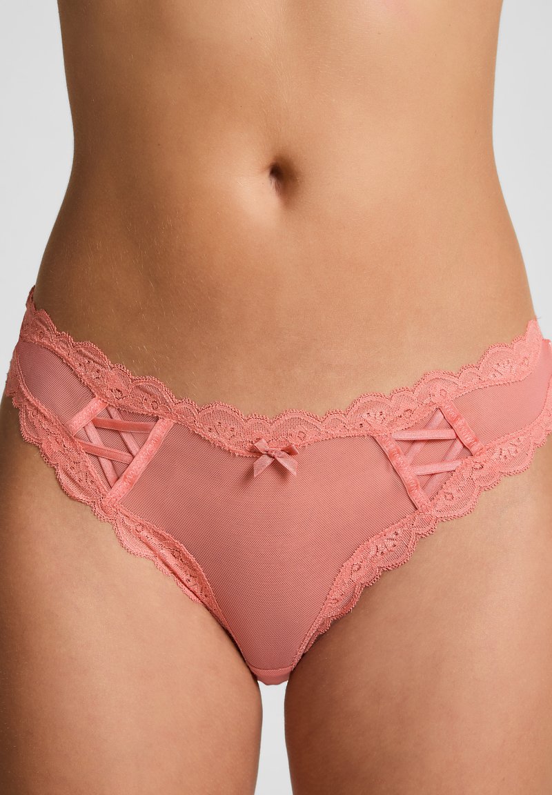 Roze kanten lingerie met lintaccenten, voorzien van een doorschijnend gaaspaneel en golvende randen. Decoratieve kruisvormige details aan de zijkanten.