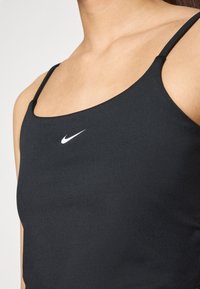 Crni sportski majica bez rukava s uskim naramenicama, s malim bijelim Nike logom na prsima. Glatka tekstura tkanine, oblik blizu tijela.