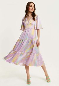 Light purple dress with a tiered design, featuring abstract yellow and blue patterns. Flutter sleeves and a v-neckline. Green strappy heels.