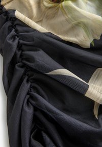 Tissu noir et beige avec des coutures élastiques froncées créant des plis texturés et des détails visibles de motif floral sur un matériau type maille.