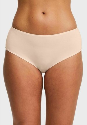 Vrouw die beige naadloze hipsterondergoed draagt, waarbij de taille, heupen en bovenbenen zichtbaar zijn tegen een effen achtergrond.