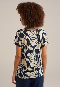 Hemd mit kurzen Ärmeln in navyblauem Hintergrund und beigen Blattmustern. Weicher, glatter Stoff mit lockerem Schnitt und hochgerollten Ärmeln.