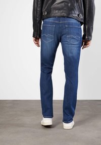 Blue denim jeans with a straight leg fit, featuring two back pockets with a pointed design and contrasting stitching. Worn with white shoes.