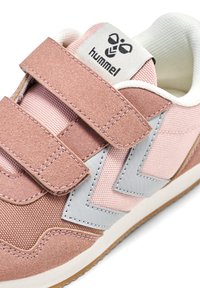 Baskets en suède rose et en mesh avec des accents en cuir gris, dotées de doubles bandes Velcro et d'une semelle en caoutchouc texturée. Logo Hummel sur la languette.