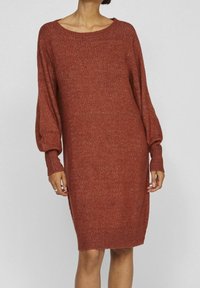 Robe pull en maille rouge rouille, dotée d'une coupe ample, d'un large col bateau et de manches longues bouffantes avec des poignets côtelés. Texture douce.