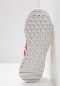 Semelle de chaussure avec un motif en nid d'abeille, en matériau en caoutchouc blanc. Forme légèrement arrondie, avec des accents en tissu rose et blanc sur les côtés.