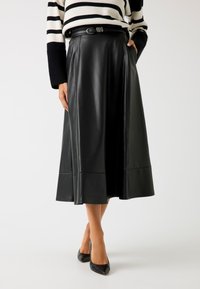 Gonna midi in pelle nera con vita aderente e cintura, caratterizzata da un design svasato e una texture liscia. Indossata con tacchi neri.