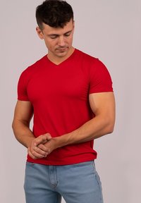 Czerwona koszulka z krótkim rękawem i dekoltem w kształcie V, wykonana z gładkiego materiału, o dopasowanym kroju, noszona z jasnoniebieskimi dżinsami, prezentująca jednolity kolor bez wzorów.