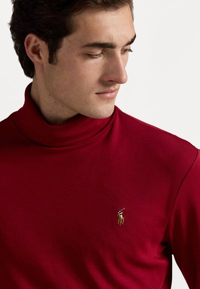 Červený rolák z jemného materiálu s priliehavým strihom. Obsahuje vyšitý logo v zlatej farbe na ľavej hrudi.