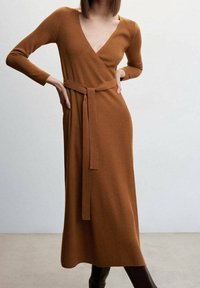 Robe à manches longues en jersey côtelé, couleur marron chaud. Équipée d'un décolleté en V profond et d'une ceinture assortie à la taille. Silhouette en A avec une longueur mi-mollet.