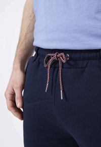 Jogging en bleu marine avec une taille à cordon, présentant des rayures rouges et blanches, des poches latérales et une texture douce et lisse.
