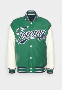 Casaco bomber verde com mangas brancas, apresentando "Tommy" em grande escrita branca, punhos canelados e colarinho e barra contrastantes em riscas.