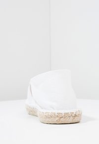 White canvas espadrille with a rounded back, featuring a woven jute sole and stitched accents along the edge for added detail.
