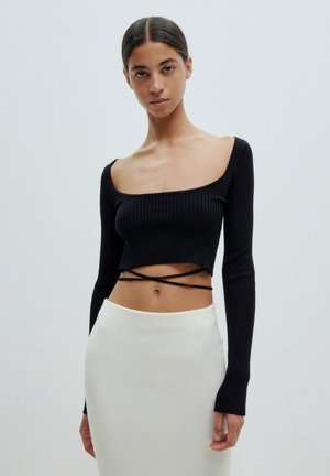 Zwart geribbeld crop top met lange mouwen, vierkante hals en crisscross banddetail. Gepaard met een witte, aansluitende rok. Soepele textuur.
