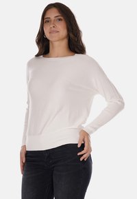 Maglione bianco a maglia con scollo ampio e orlo a coste, abbinato a jeans neri, con maniche lunghe e vestibilità rilassata.