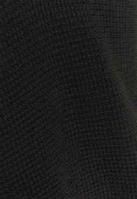 Tissu noir texturé avec un motif en nid d'abeille, présentant une apparence douce et légèrement duveteuse. La surface est uniforme et régulière.