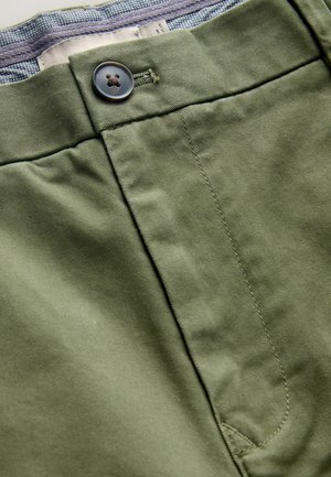 Olivgrüne Hose mit Knopfverschluss, aus glattem Baumwollstoff und einer subtilen Textur, mit kontrastierendem Futter in einem blau-weißen Muster.