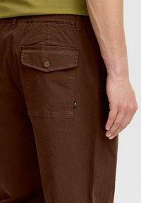 Braune Baumwollhose mit entspannter Passform, ausgestattet mit einer geknöpften Gesäßtasche, elastischem Bund und einem kleinen Markentags.