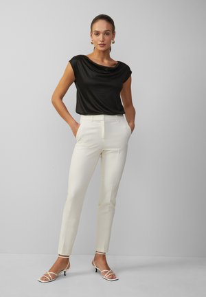 Haut en satin noir à manches courtes associé à un pantalon crème sur mesure et des escarpins blancs à lanières, avec une silhouette ajustée et une texture lisse.
