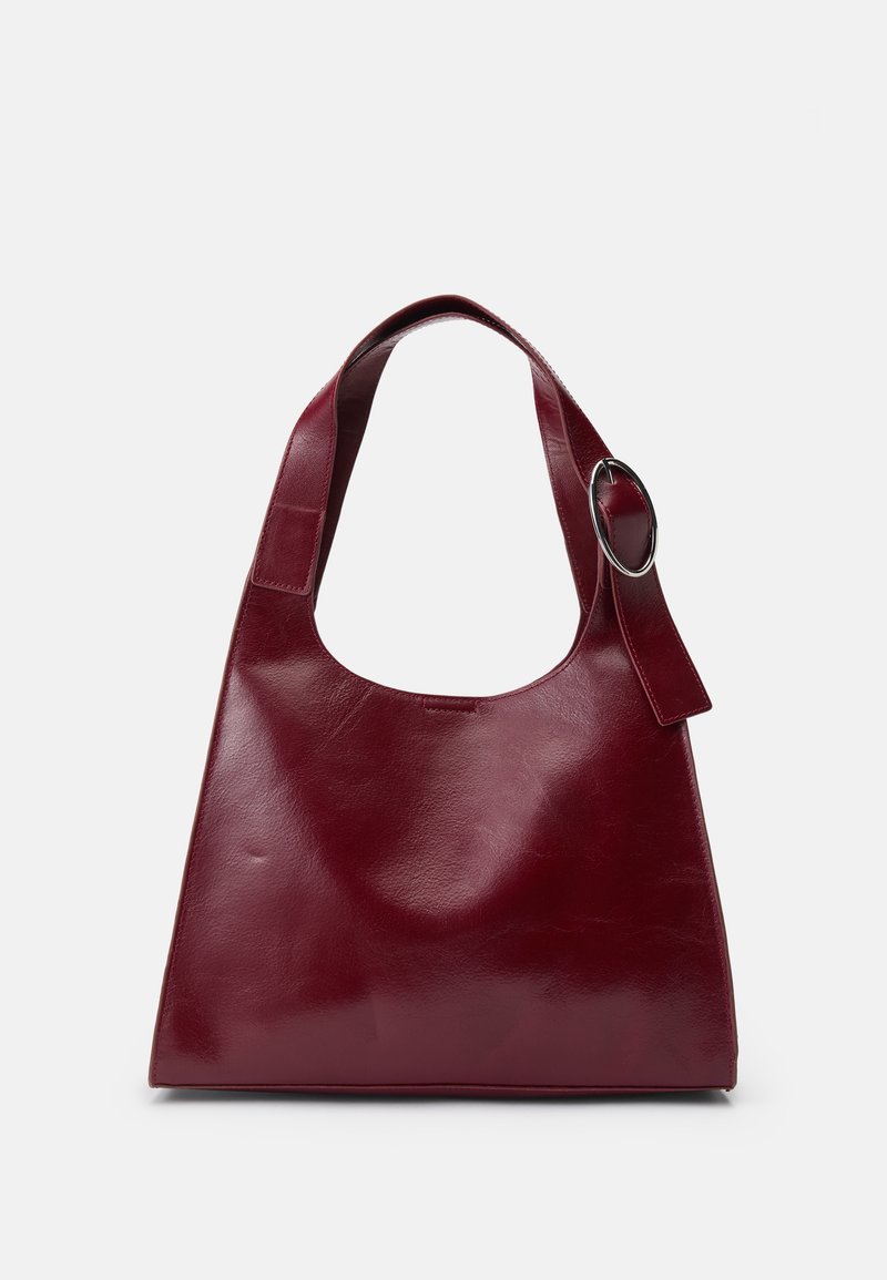Geantă de umăr din piele burgundy, cu o textură moale și netedă, având o curea lată și un accent metalic sub formă de inel. Design minimalist.