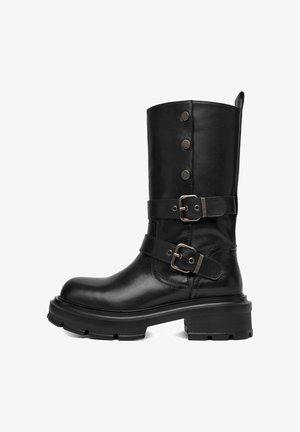 Botas negras de cuero hasta la rodilla con dos correas ajustables con hebillas plateadas, botones de presión decorativos y una suela gruesa y texturizada.