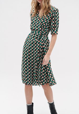 Vestido de manga larga en una tela negra con un patrón geométrico en verde, rojo y blanco. Cintura ajustada con una falda fluida.