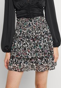 Falda negra con estampado floral y volantes en capas. Presenta una cinturilla fruncida y colores vibrantes en patrones florales sobre un fondo blanco.