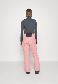 Damen Roxy Skianzug, bestehend aus einem figurbetonten dunklen Oberteil und lockeren rosa Hosen mit einem strukturierten schwarzen Rückenpaneel und Roxy-Logo an der Seite.