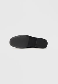 Talpa neagră a unei pantofi eleganți pentru bărbați, cu vârf pătrat și călcâi texturat, expusă pe un fundal alb simplu.