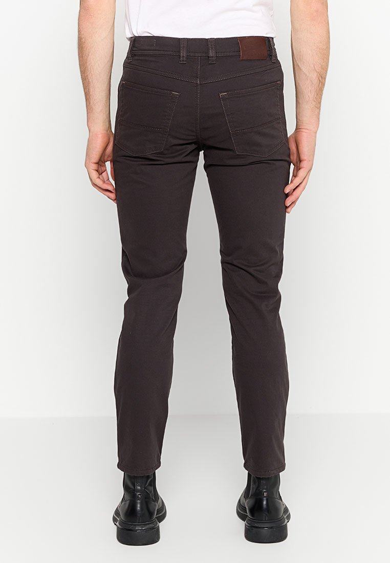 Brązowe spodnie slim-fit o gładkiej fakturze, z dwiema tylnymi kieszeniami i brązową skórzaną łatą w talii, noszone z czarnymi butami.
