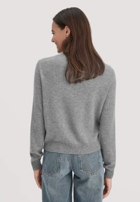 Grauer gestrickter Pullover mit rundem Halsausschnitt, gerippten Bündchen und Saum. Getragen mit hochtaillierten blauen Jeans, die eine lockere Passform zeigen.