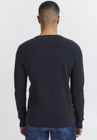 Mørkeblå strikket sweater med ribbet tekstur, rund halsudskæring og lange ærmer. Kanten og manchetterne er afsluttet med en glat strik.