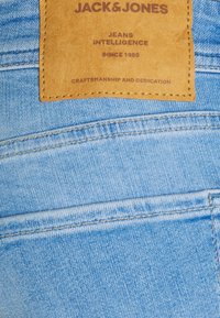 Tela de mezclilla azul claro con una etiqueta de cuero adjunta, que presenta texto en relieve: "JACK & JONES", "JEANS INTELLIGENCE" y "SINCE 1990".