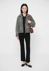 Sivá vyšívaná bunda s golierovým dizajnom, skombinovaná s čiernou košeľou a zvonovými čiernymi nohavicami. Príslušenstvo tvorí hnedá kabelka.