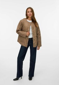 Vadderad tan-färgad jacka med rund halsringning och knäppning, i kombination med mörkblå vida jeans och svarta klackstövlar. Slät textur.