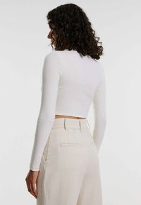 Weißes geripptes Langarm-Crop-Top, eng anliegendes Design. Kombiniert mit hoch taillierten hellbeigen Hosen mit Gesäßtaschen und einer glatten Textur.