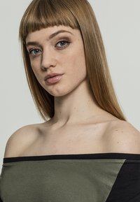 Off-the-shoulder viršus su juodu juostele ir alyvuogių žalios spalvos įsiuvais. Minkšta, lygi medžiaga; kasdienis dizainas; be raštų ar metalinių detalių.