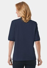 Dunkelblaues Kurzarmhemd mit rundem Kragen, weicher Textur und lockerer Passform. Sichtbare umgeschlagene Manschetten und schlichtes Design.