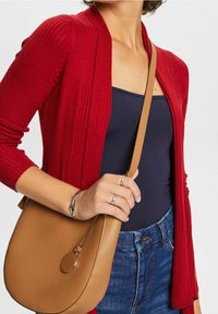 Rød ribbet cardigan, navy top og denim jeans. Brun crossover-taske med rund hardwaredetalje og glat tekstur. Casual outfit-elementer.