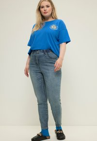 Camiseta de algodón azul con un gráfico de sol, combinada con unos jeans de tiro alto en lavado claro y mocasines negros con un detalle de cadena dorada.
