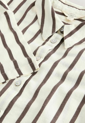 Chemise en lin à boutons présentant des rayures alternées crème et marron, un col et des boutons clairs. Tissu doux et texturé.