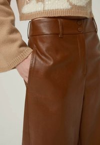 Pantaloni in finta pelle marrone con vita alta, caratterizzati da due bottoni in vita e tasche laterali, texture liscia e vestibilità sartoriale.