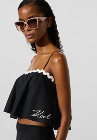 Fekete, rövidített felső fehér hullámos szegéllyel és a szegélyén hímzett "Karl" logóval. A modell túlméretezett, rózsaszínes napszemüveget visel.