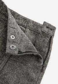 Tkanina s vzorom houndstooth v odtieňoch čiernej a bielej. Obsahuje zapínanie na gombík a zips s ohnutým pásom.