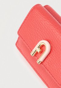 Korallikarva tekstuuriga nahast rahakott valgel taustal, millel on kuldse ja helesinise U-kujulise metallist kinnitus.